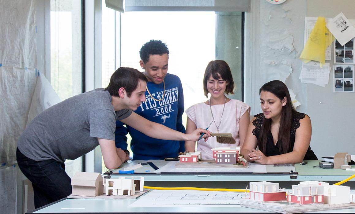 Students stand and sit around a drafting table looking at their project