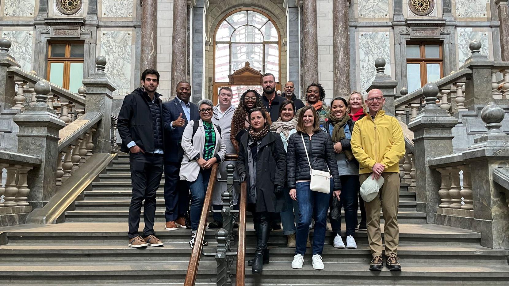 15 EMBA students stand on the steps of an old stone building