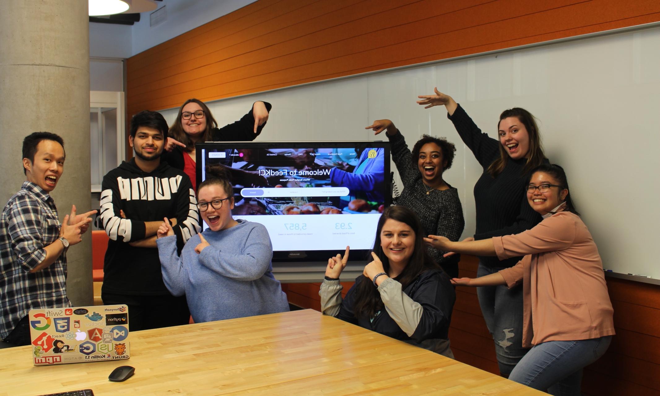 group photo of Enactus team in front of screen that shows their new app