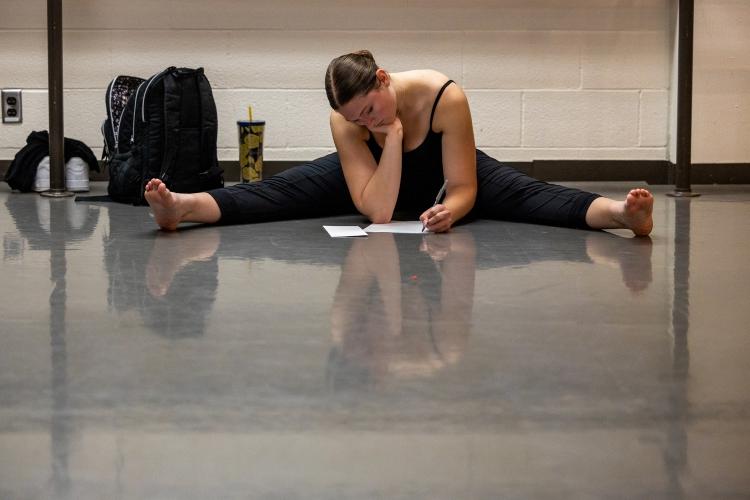 A dancer sits on the floor doing the splits writing with her chin resting in her hand