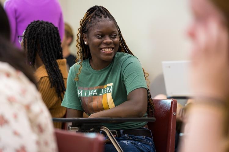 A student sits at a desk smiling