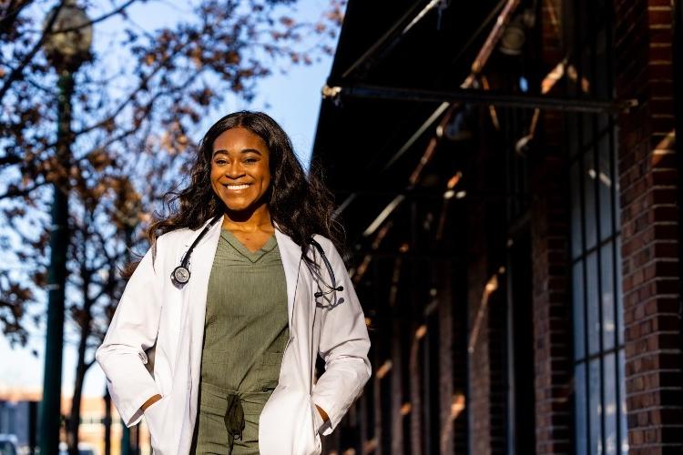 Dumebi Okocha, a student in the accelerated B.A./M.D. program, posing outside in a white coat. 