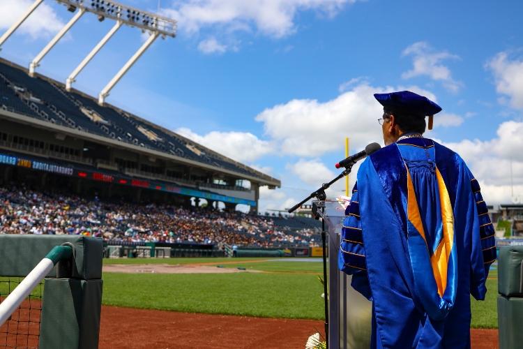 Chancellor Agrawal stands at a podium on the field of Kauffman Stadium with the stands in the background