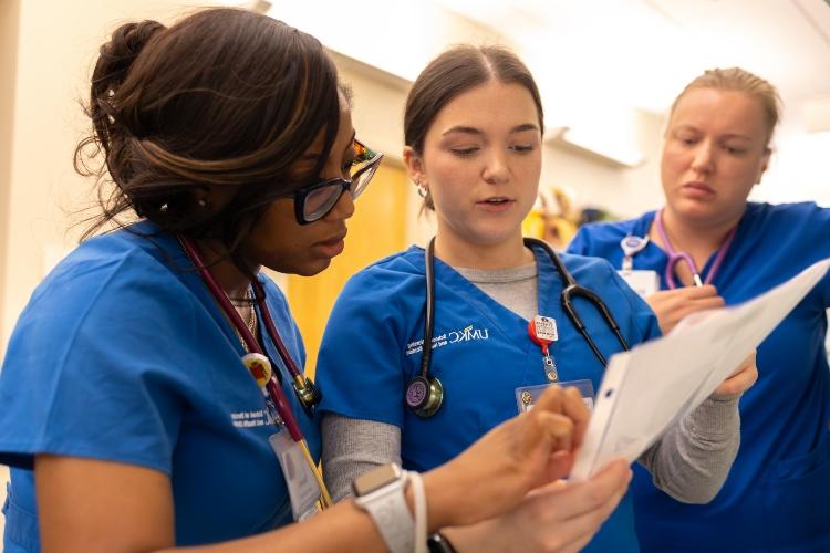 Tatyana Charles stands with two other nursing students discussing a simulation case and referring to a document